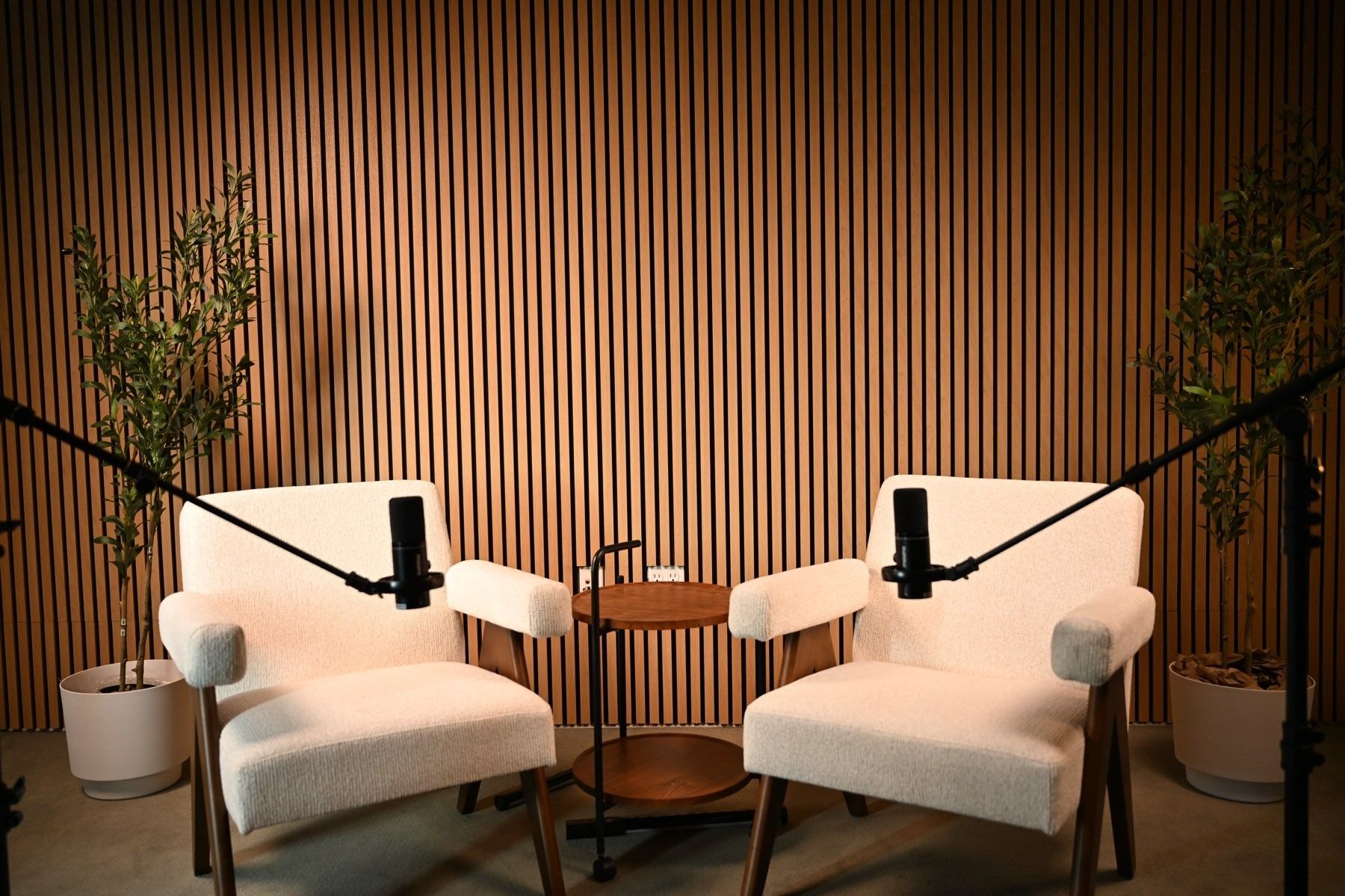 The podcast set at Axeom Content Studio in Dallas, Texas: two cream chairs, microphones on booms and a wood slat wall